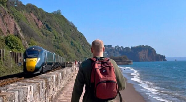 Man walking the sea wall at Teignmouth with train on left and sea on right