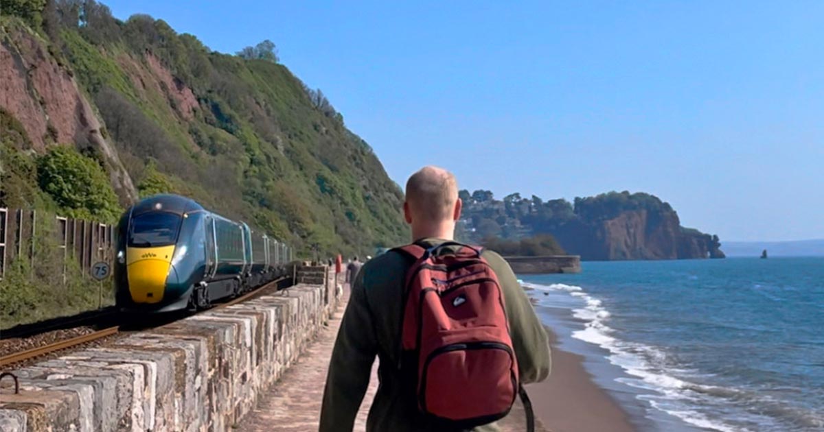 Man walking the sea wall at Teignmouth with train on left and sea on right