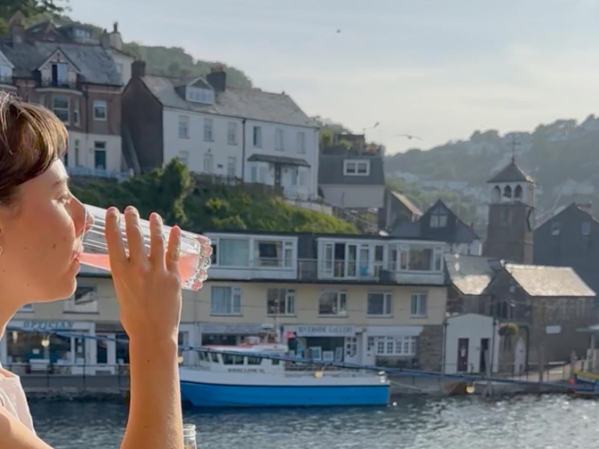 Woman having a drink while looking out across Looe’s harbour
